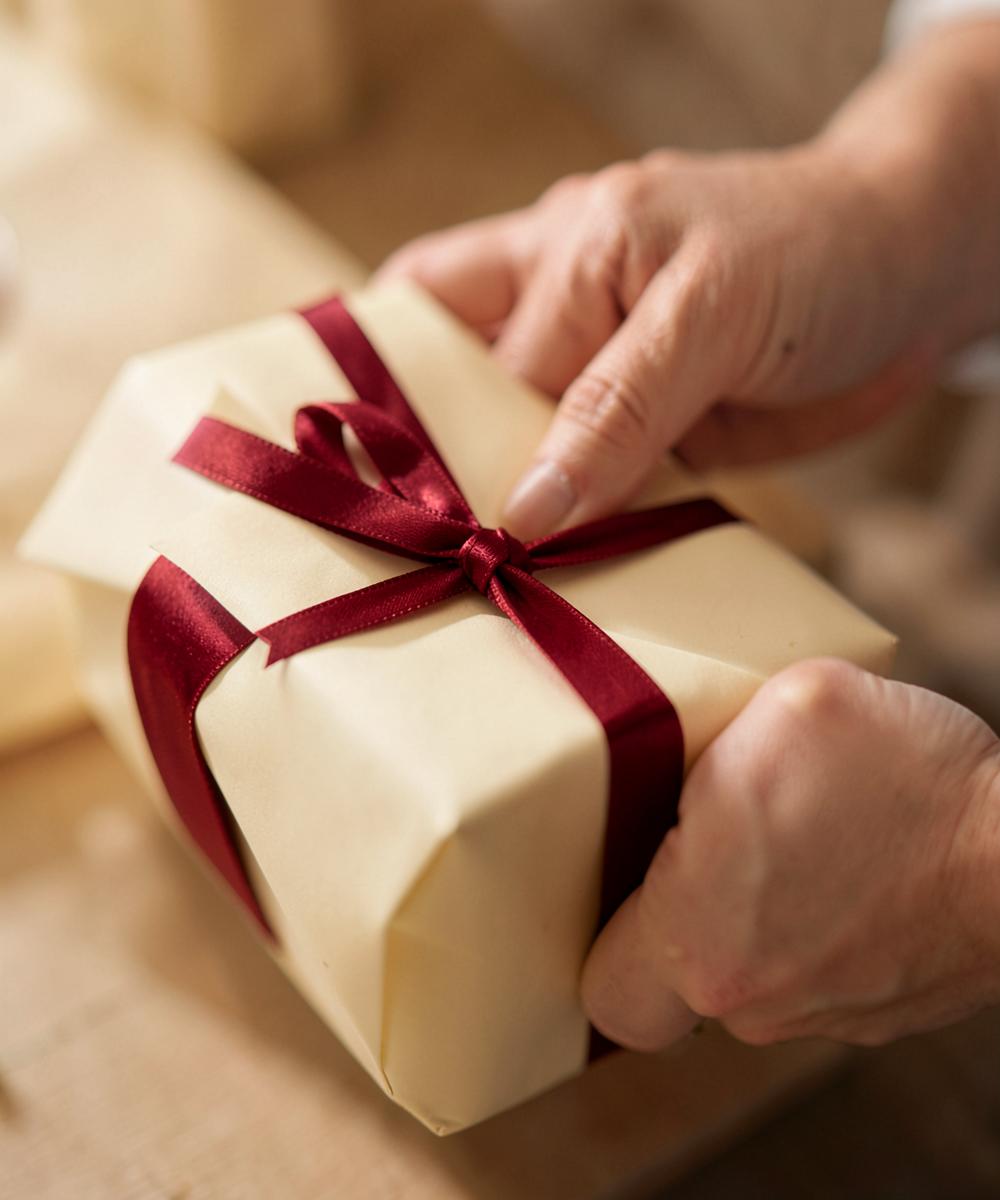 Hands tying a burgundy ribbon around a cream wrapped gift