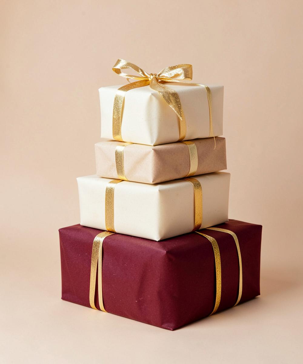 A stack of gifts wrapped in cream, sand and burgundy with gold ribbon